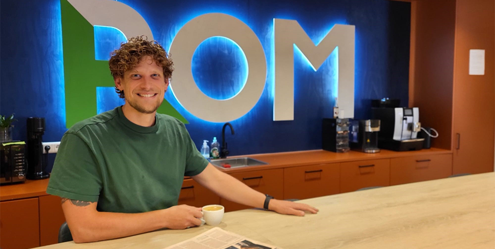 foto van een man met een koffie kopje met de letter POM achter zich